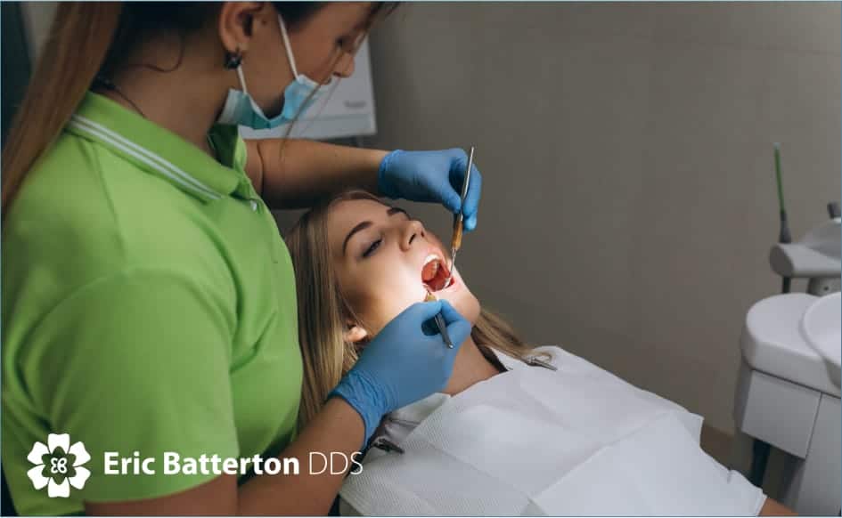 Patient sitting in a dentist's chair during a routine check-up, with the dentist examining their teeth for cavities using a dental mirror and explorer tool.